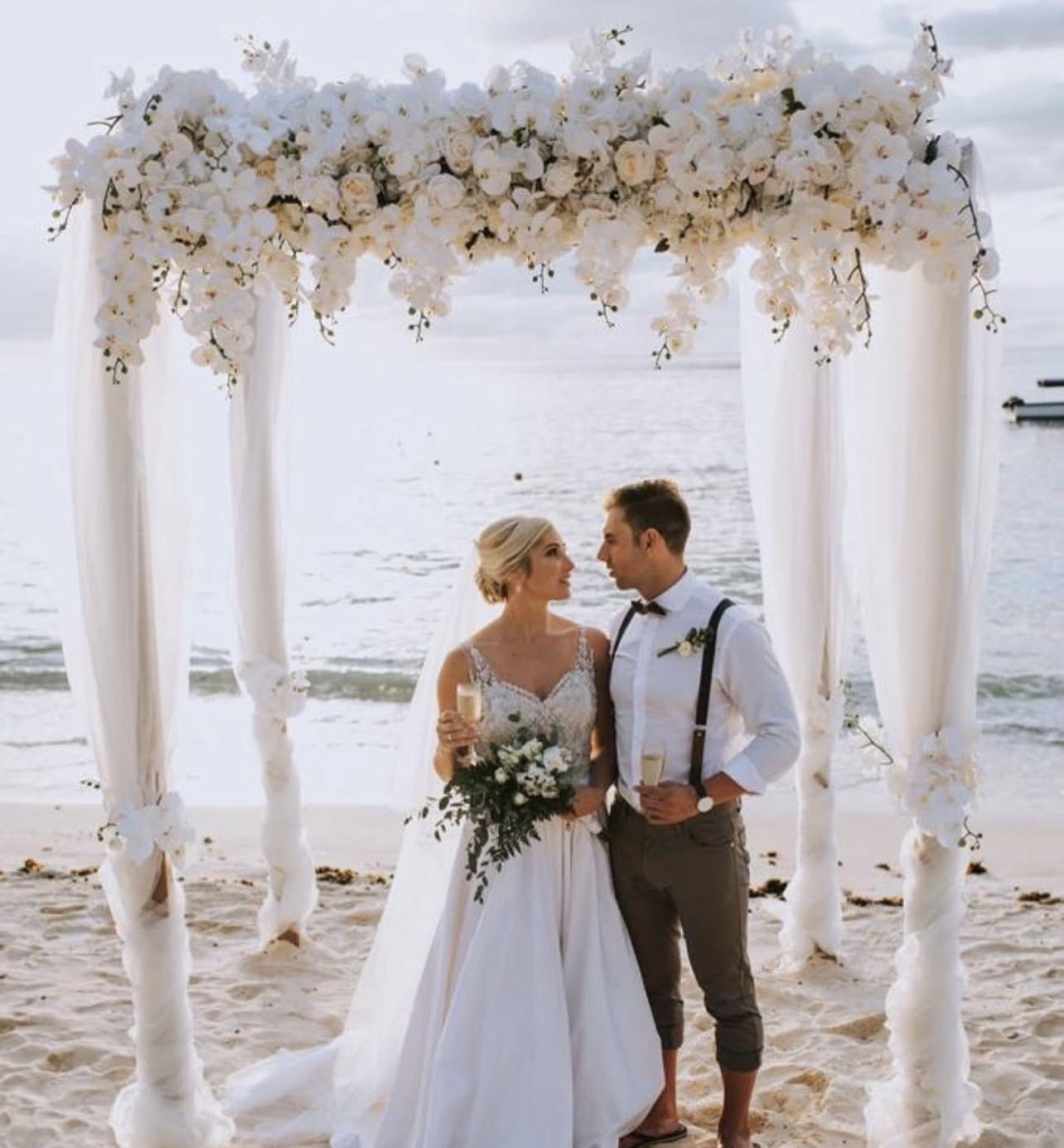 Beach ceremony with a white floral arch and the sea behind