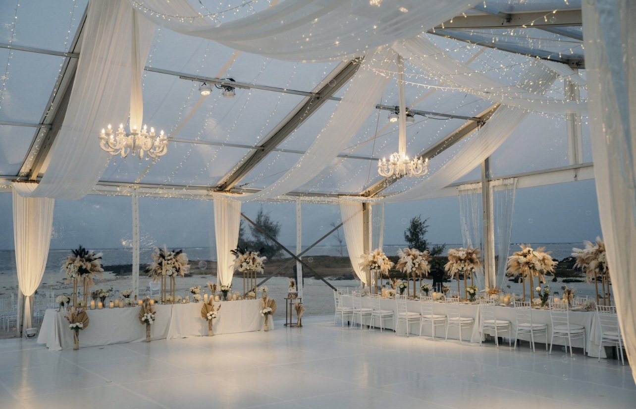 Clear-roof marquee reception lit at dusk with hanging florals